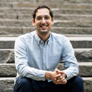 A photo of a man wearing a light blue shirt and sitting outside on stairs