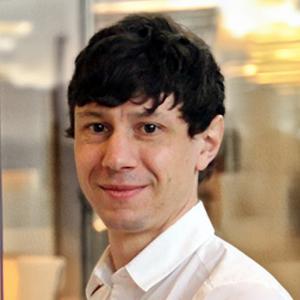 A photo of young man with dark brown hair and brown eyes. He is wearing a white shirt.