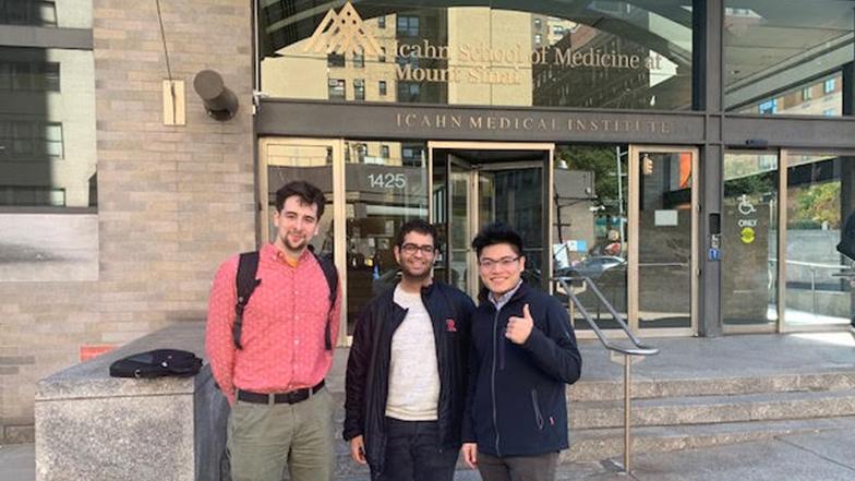 Three students stand infront of a building