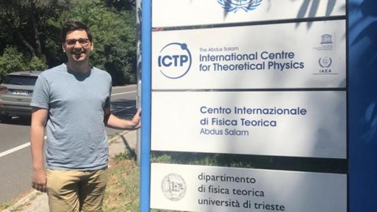 Zane Martin posing by the entrance sign to the International Centre for Theoretical Physics