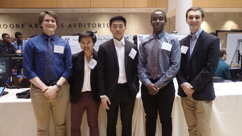 Five students (four males and one female) stand in a row
