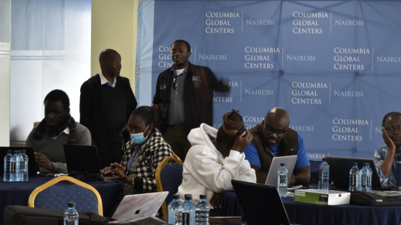 7 conference participants are sitting at tables or standing and collaborating in the break room