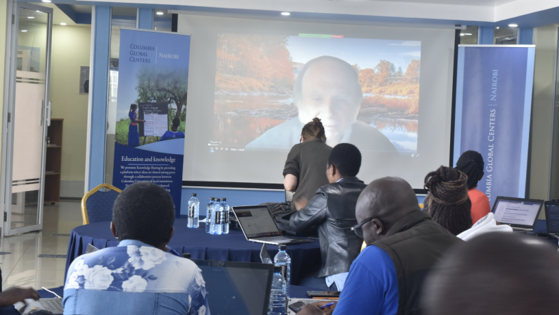 Conference participants sitting in a room watching a virtual presentation