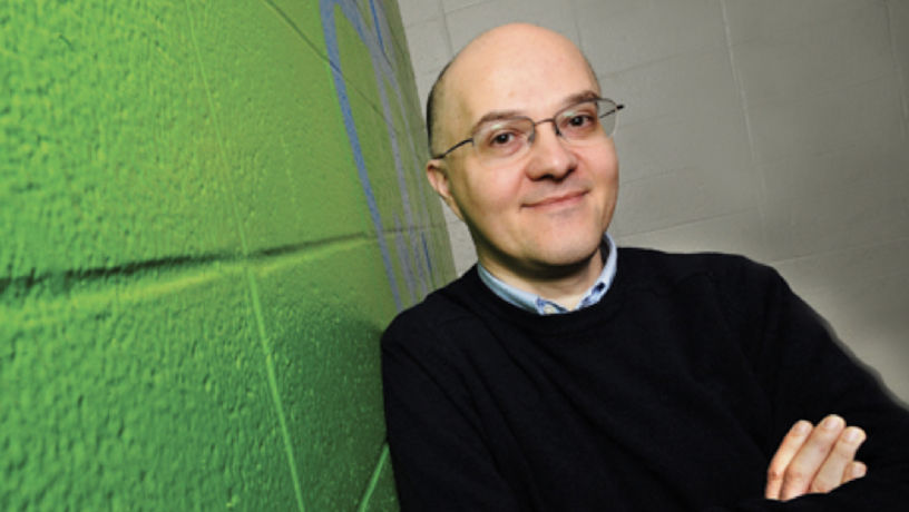 Photo of Professor Lorenzo Polvani leaning aginst a green wall. He is wearing a black sweater. He is smiling and has his arms folded across his chest.