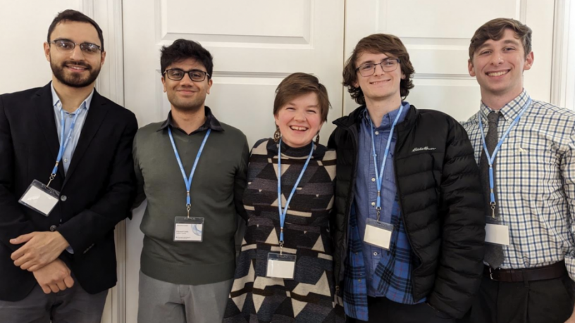 Five students standing in a line. They are smiling and wearing name badges.