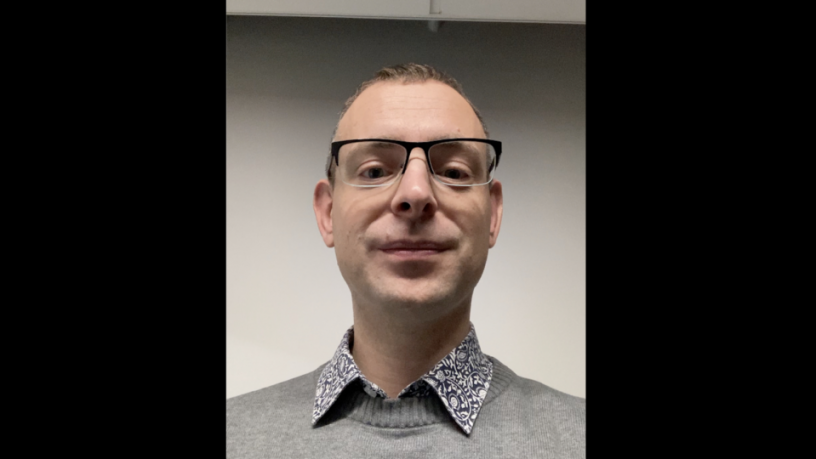 Photo of Dr. Jacek Aleksander Gruca is a current Fulbright Visiting Research Scholar. He is wearing a grey sweater and printed shirt. He is wearing glasses and smiling.