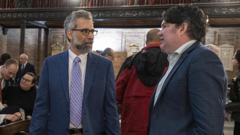 Two men wearing blue suits are standing and talking