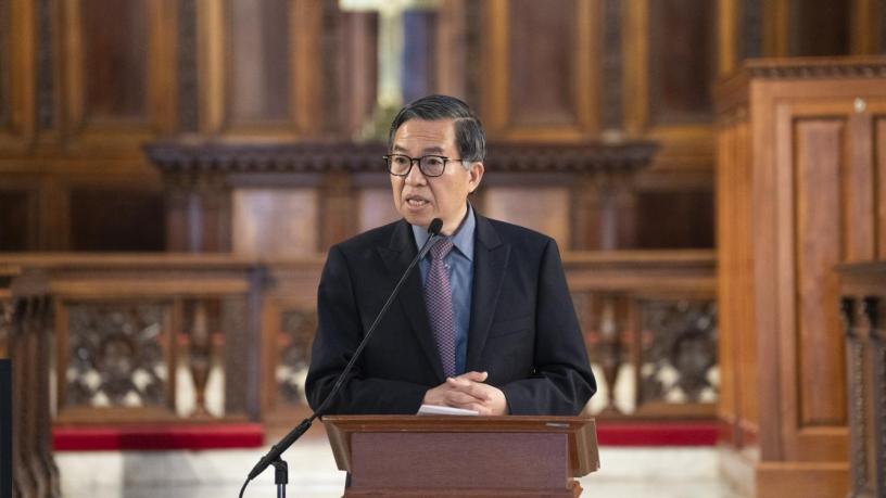 A photo of Dean Shih-Fu Chang. He is wearing a blue suit and tie and is standing at a podium in the front of a chapel