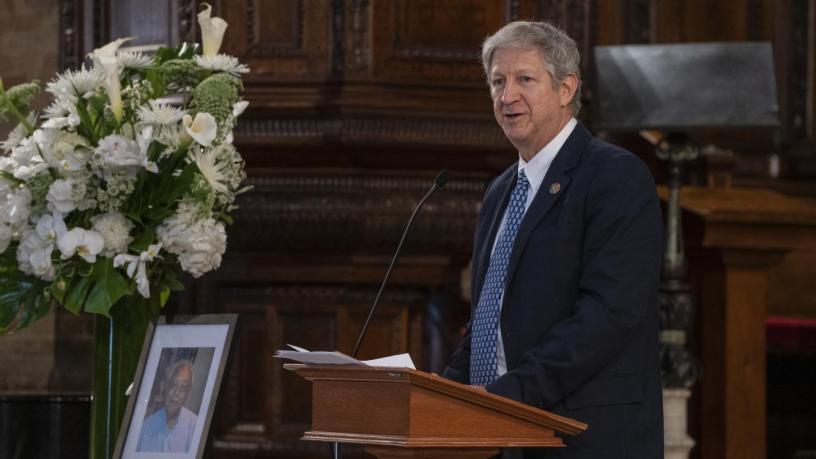 A photo of Prof. David Keyes. He is wearing a black suit and tie and is standing at a podium in the front of a chapel.