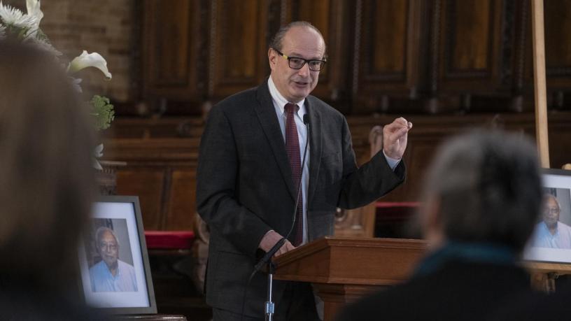 A photo of Dr. Yurij Baransky. He is wearing a grey suit and tie and is standing at a podium in the front of a chapel.