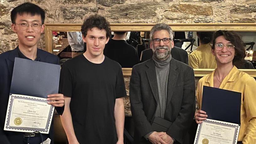 Three students holding awards and standing with a faculty member.