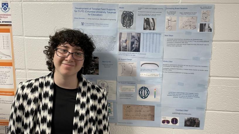 A student stands in front of their research poster