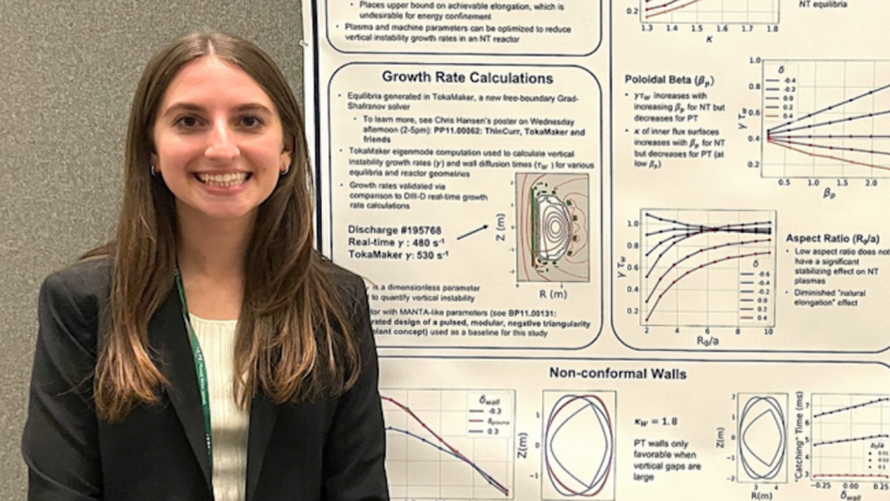 A young white woman with long brown hair stands in front of a research poster. She is wearing a black jacket.