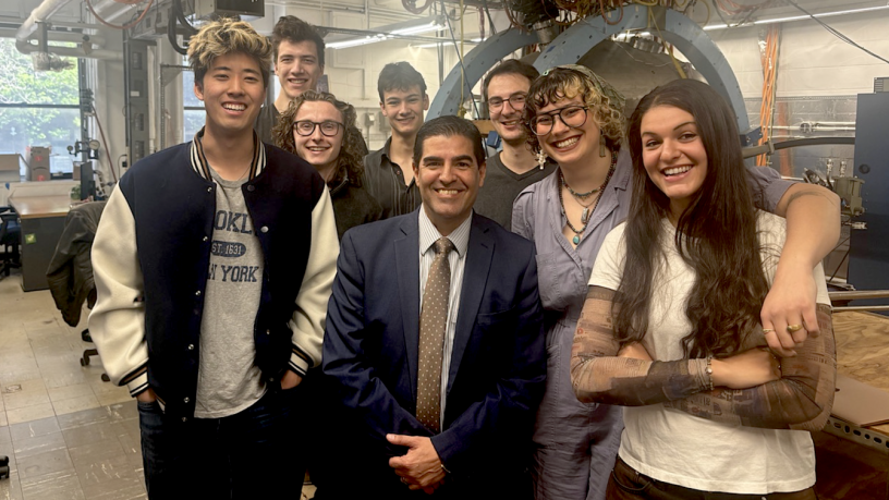A group of college students and a middle aged man stand in a lab