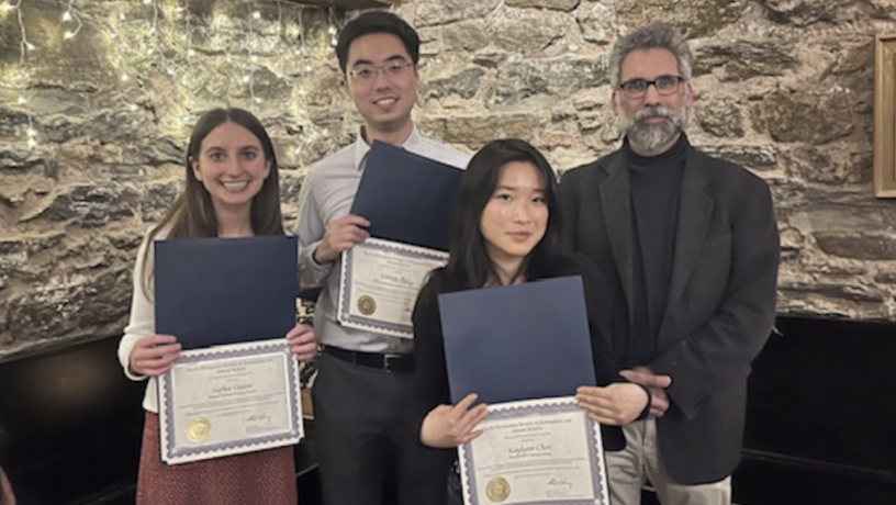 Three students and one faculty member stand in a row. They students are holding award certificates.