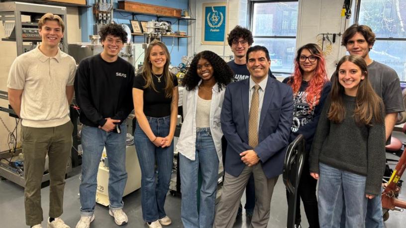 A group of college students and a middle aged man stand in a lab