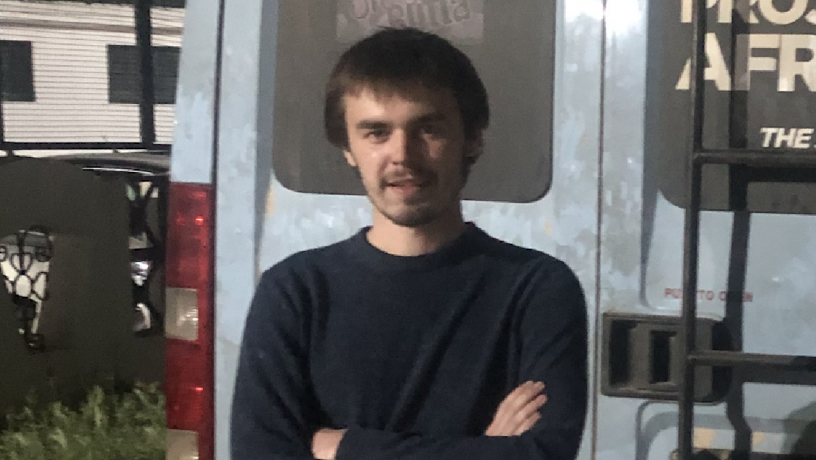 A young man stands outside and is wearing a black shirt
