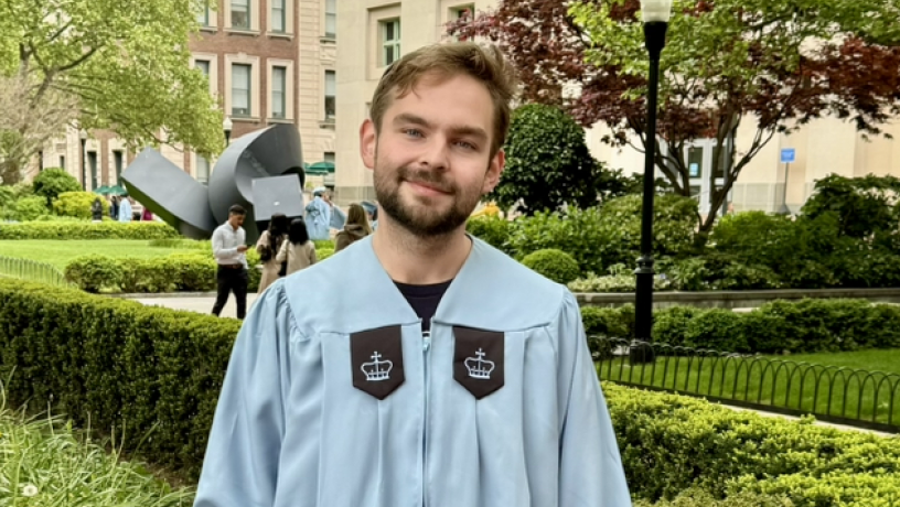 A young man stands outside wearing light blue commencement regalia