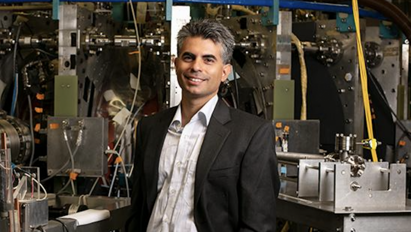 A photo of a middle aged man with brown and gray hair. He is standing in a lab and wearing a suit coat and white shirt.