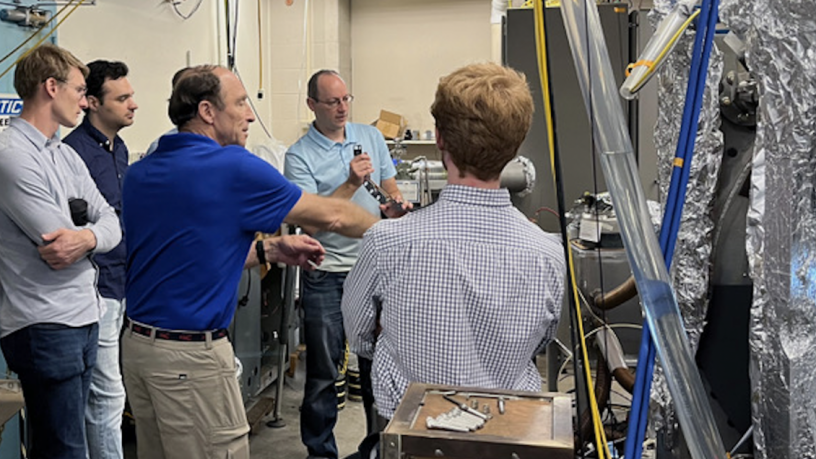 A group of people are standing in a lab and looking at an experiment.