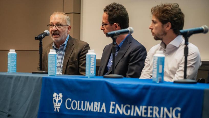people sit at a panelist table and speak into microphones