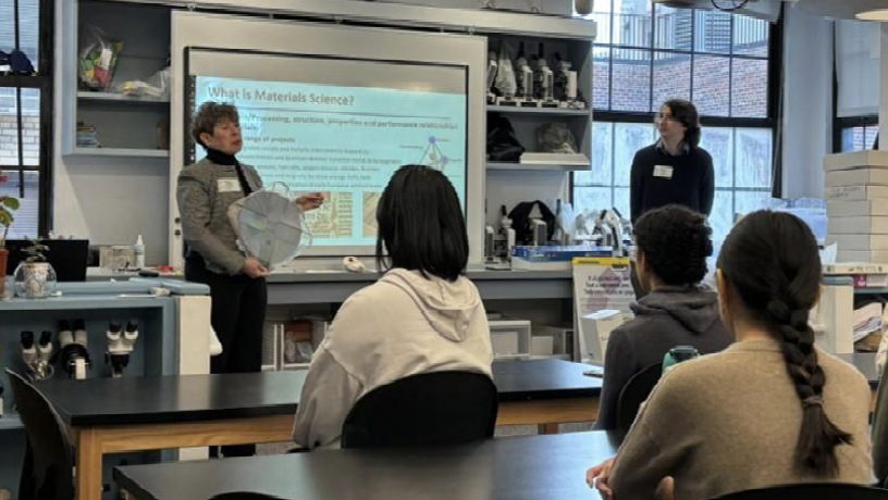 Two people stand in front of a classroom giving a lecture