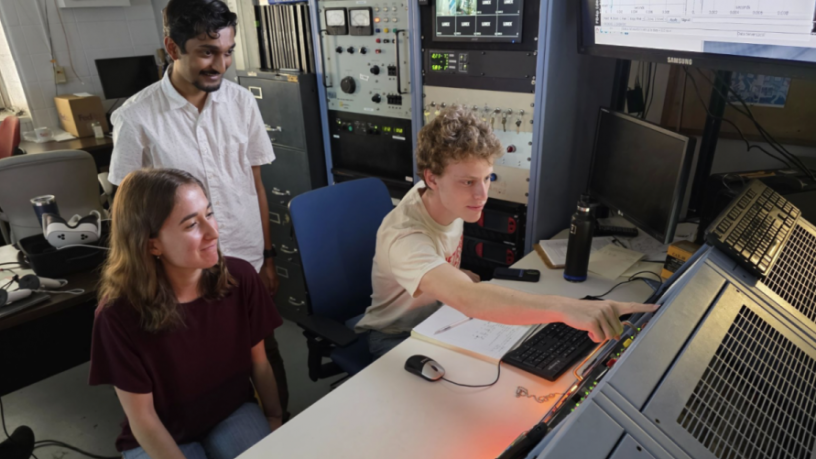 Three students operate a control panel in a lab