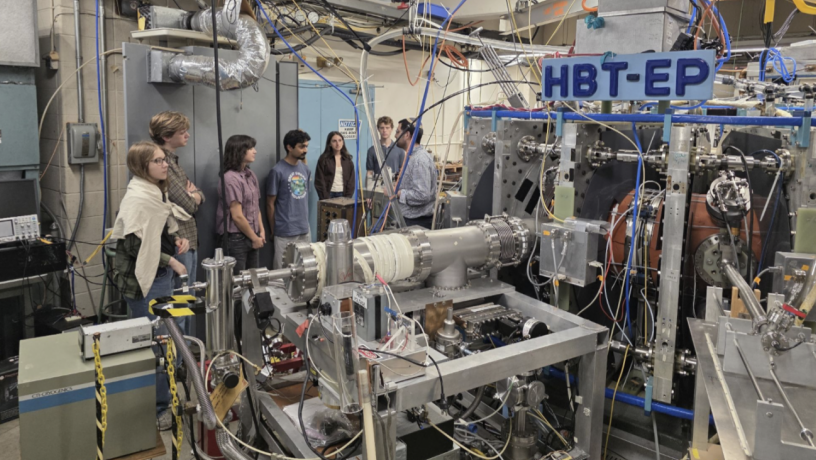 A group of students stand in the HBT-EP lab which is full of machinery