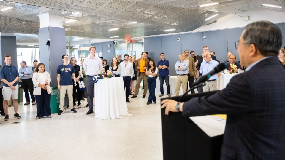 Dean Shih-Fu Chang addresses a group of guests from a podium in a brightly lit event space.